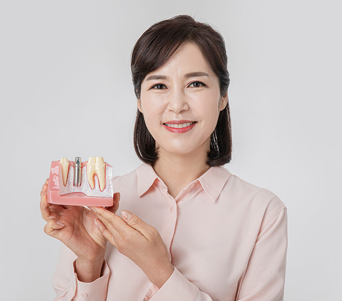 임플란트 모형을 들고 웃고 있는 중년 여성 환자